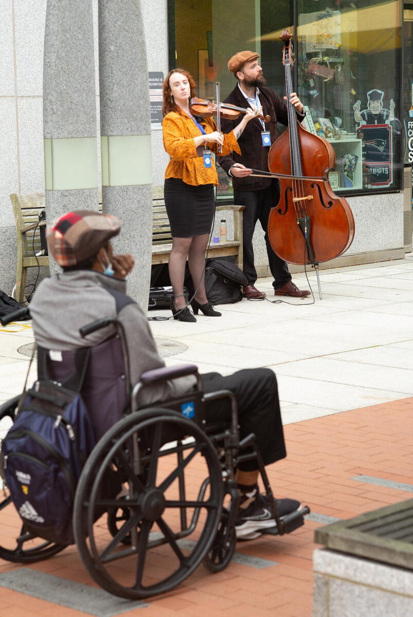 a man in a wheelchair watches a violinist and celloist perform