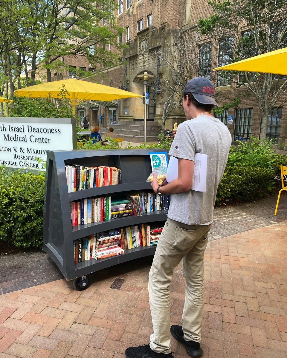 a man in a hat checks out a book at a small outdoor library